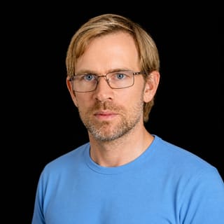AI-generated portrait of Alex Kerss wearing an AI Videos-blue top against a black background.