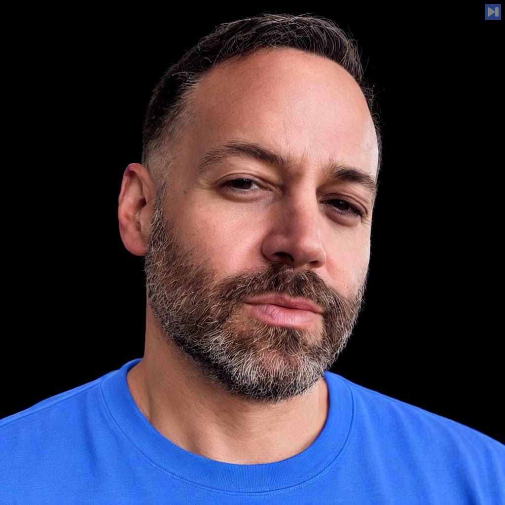 Head-and-shoulders portrait of James Poulos wearing a blue T-shirt against a black background.