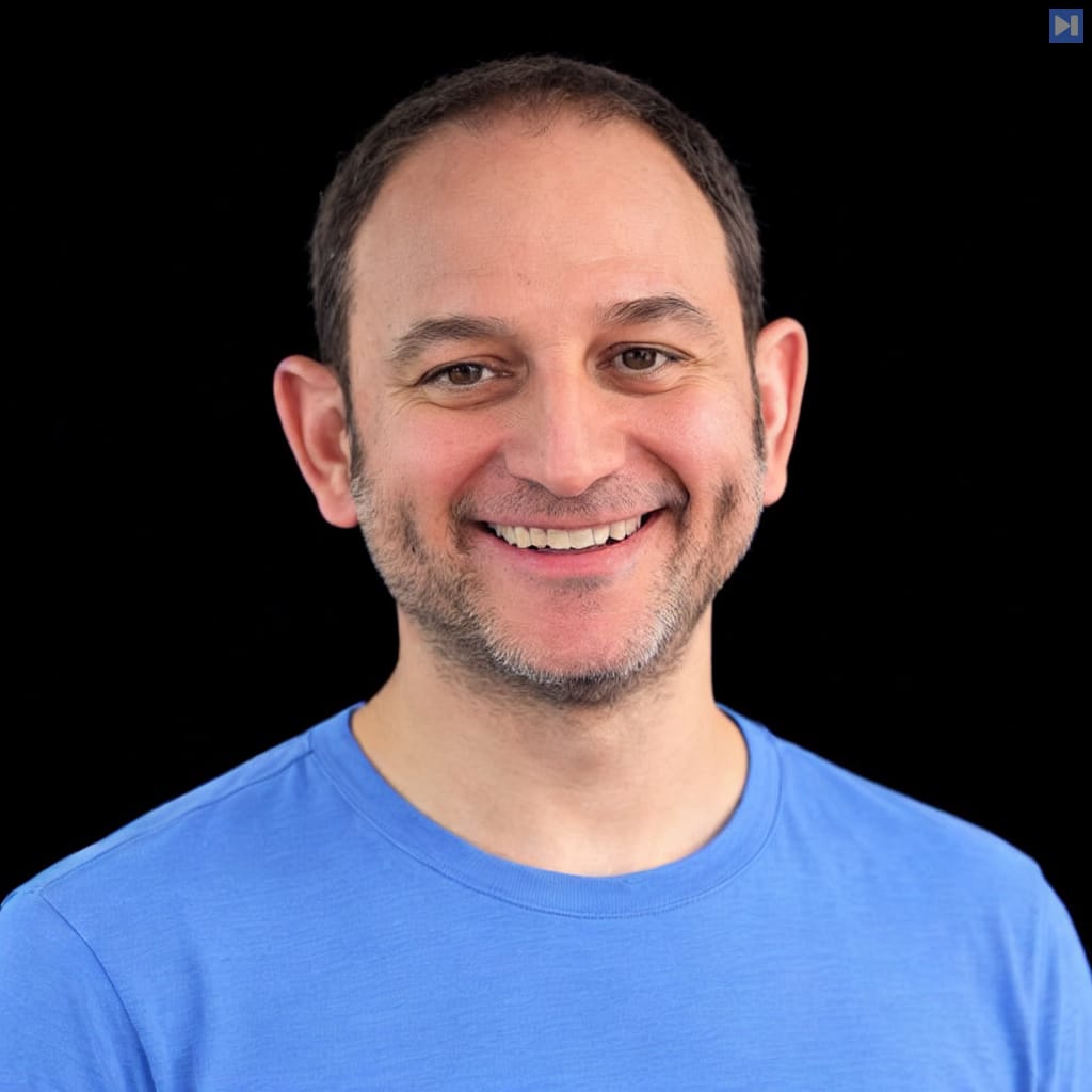 Head-and-shoulders portrait of Noam Shazeer in a light blue top against a black background.