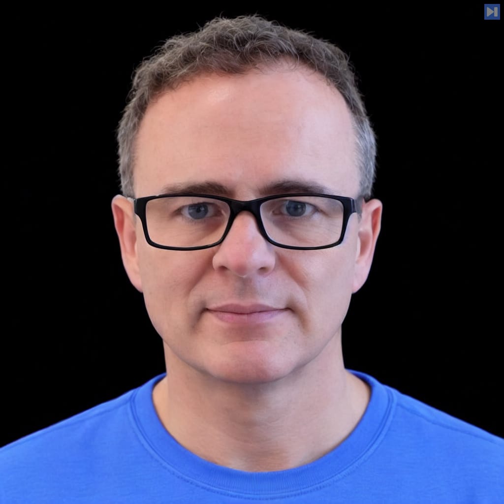 Head-and-shoulders portrait of Shane Legg with short curly greying hair and black rectangular glasses, wearing a light blue crew-neck top against black.