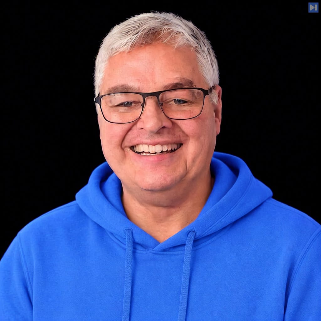 Tim Tyler smiles wearing dark glasses and a blue hoodie against a black background.